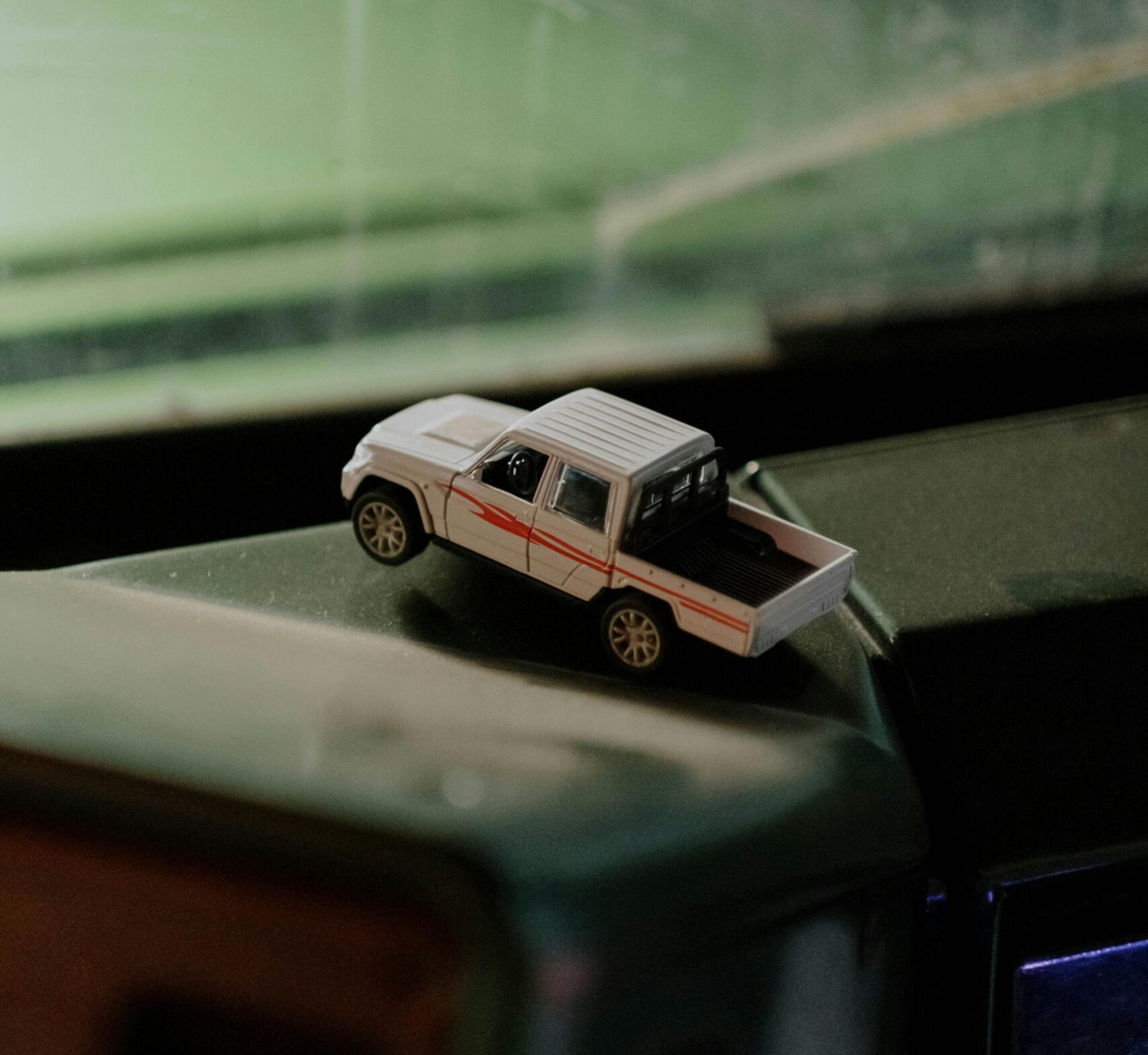 A toy truck rests on a dusty vehicle dashboard inside a car.